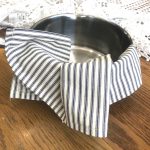 Ticking stripe handmade kitchen tea towel hung on a pot on a wooden table