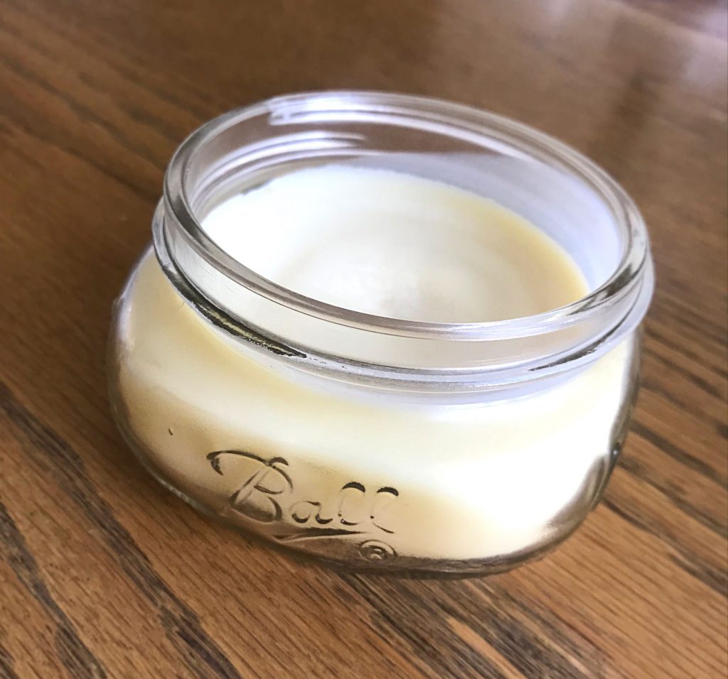 Finished homemade Shea body butter recipe in a glass jar on a wooden table