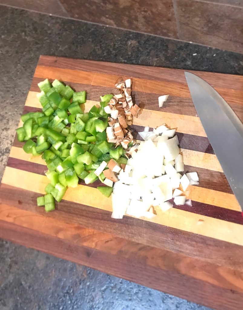 Chopped bell peppers, mushrooms, and onions on a wooden cutting board