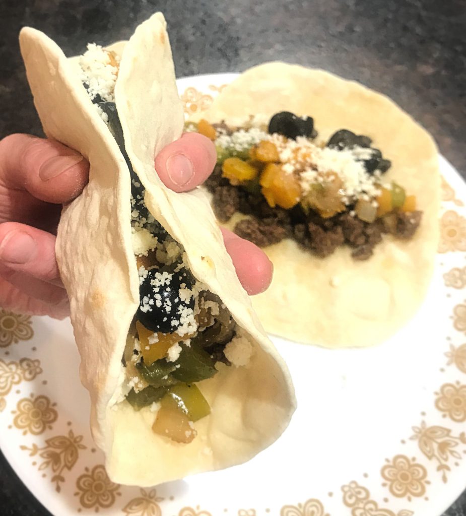 One taco rolled up and one laying flat on a plate
