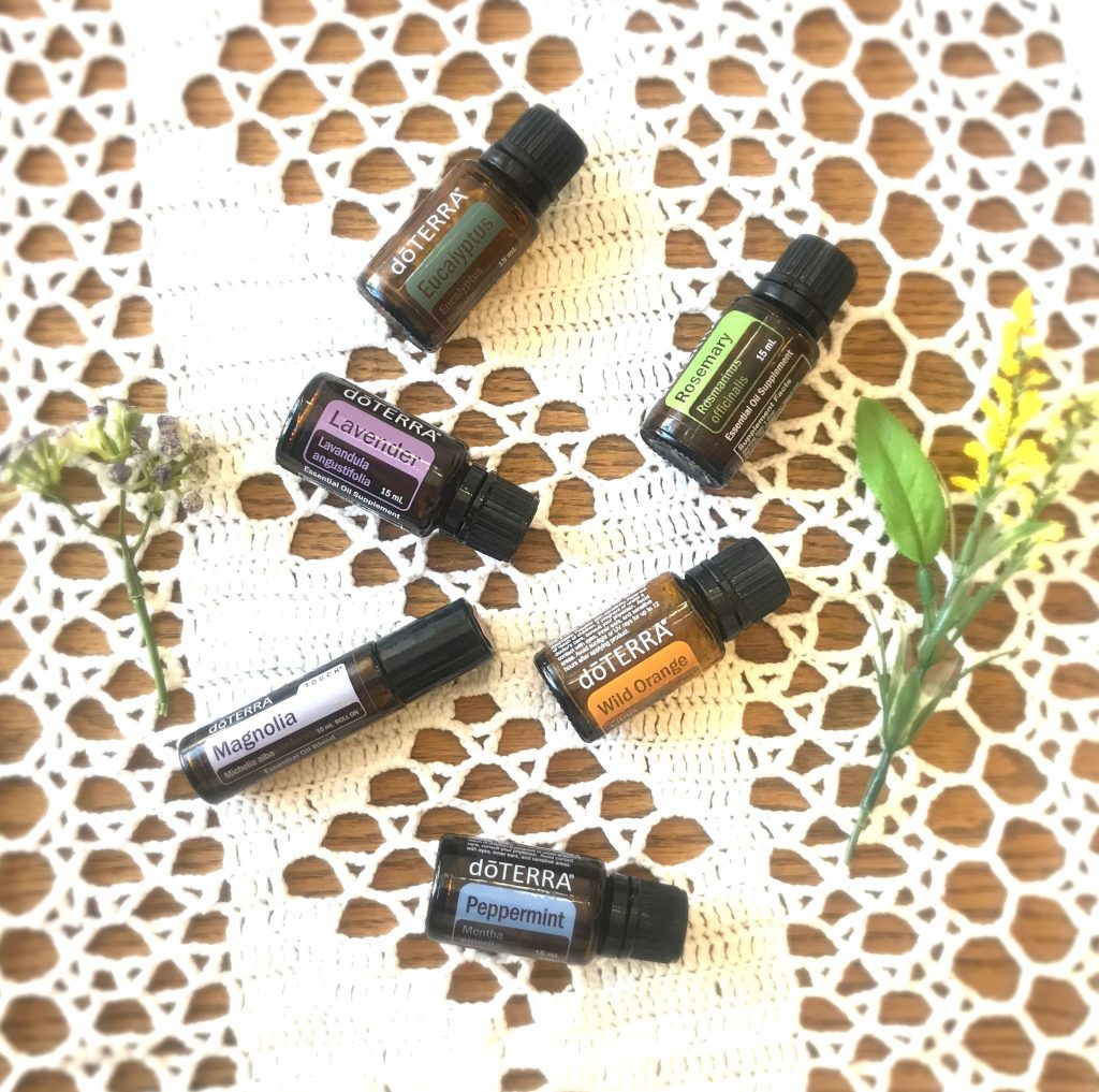 Several doTERRA Essential Oils laid out on a white table cloth with faux florals