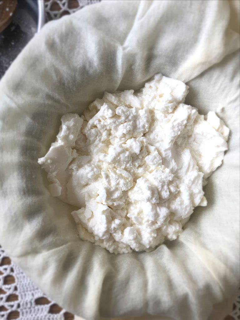 Freshly cultured homemade cream cheese curds in a muslin over a strainer and bowl