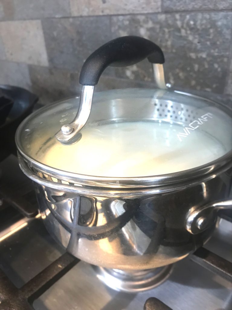 Stainless steel pot containing milk, cream, and cultures on a gas stove