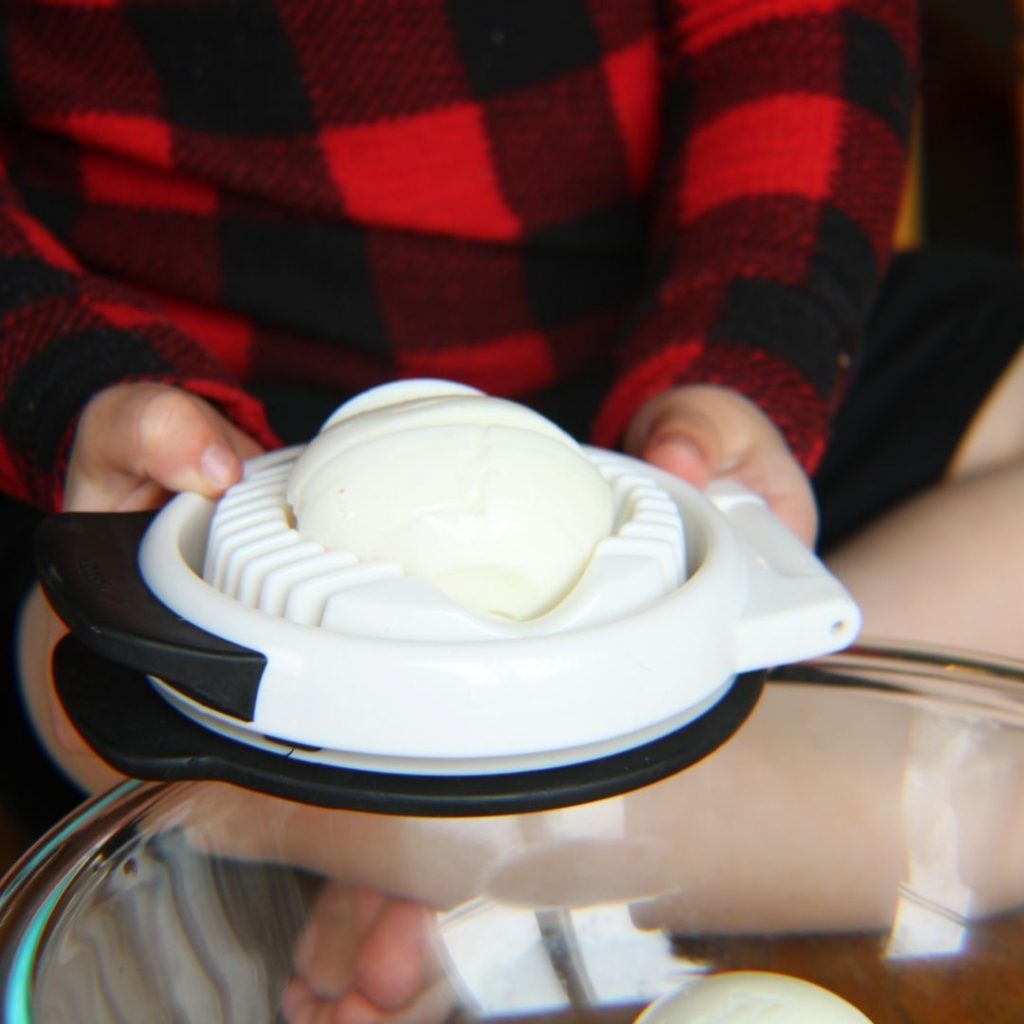 sliced, hard-boiled egg on a slicer being held by a child
