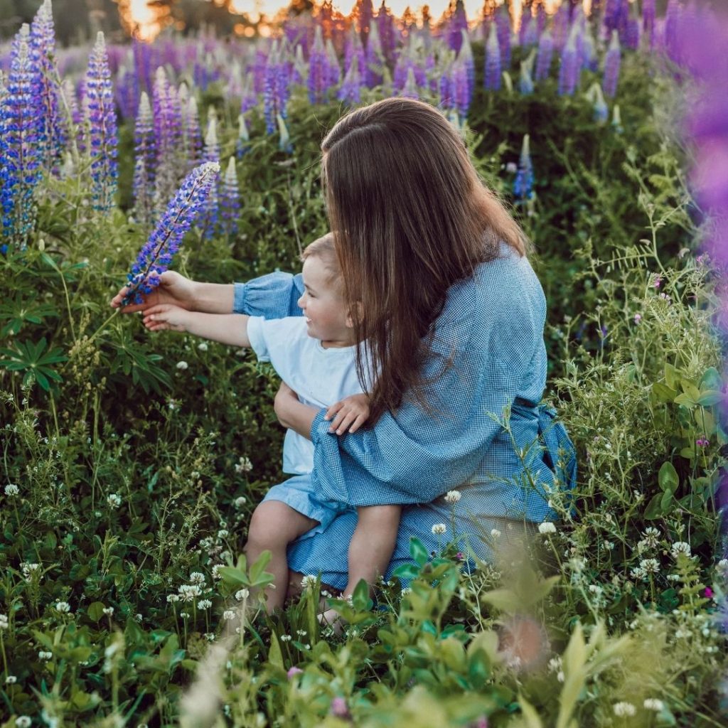 Woman sitting in a field with a boy handing him a purple flower. 
