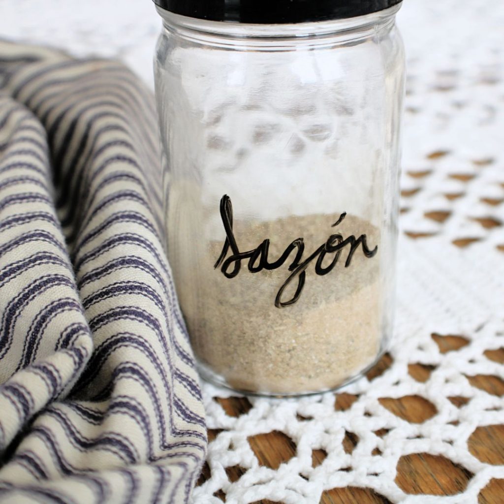 Mixed spices in a jar and labeled "Sazon" next to a ticking striped towel