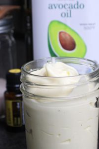 Mayonaise in a glass jar with avocado oil, salt, and Lemon Essential Oil in the background