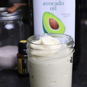 Mayonaise in a glass jar with avocado oil, salt, and Lemon Essential Oil in the background