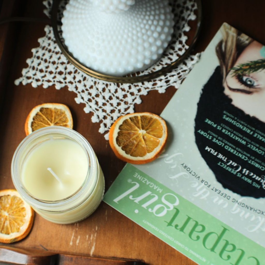 Candle, dried oranges, and a magazine on a wooden desk