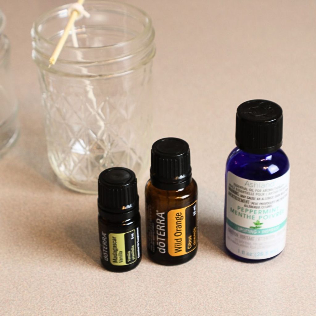 three essential oil bottles and a glass jar with a wick inside it 